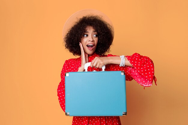 かわいい青いスーツケースを持ってアフリカの髪型で興奮している黒の女の子。
