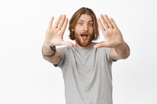 Excited blond guy look through hand frames and smiling amused, shooting, creating picture, imaging something, being inspired, standing over white background.