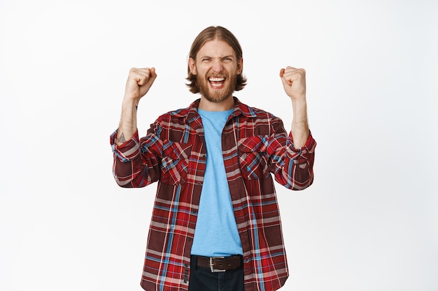 Free photo excited blond man shouting and shaking clenched fists, standing on white