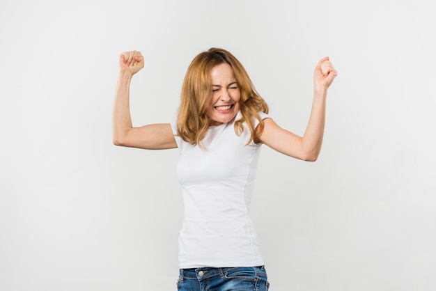 excited blonde young woman clenching her fist against white backdrop