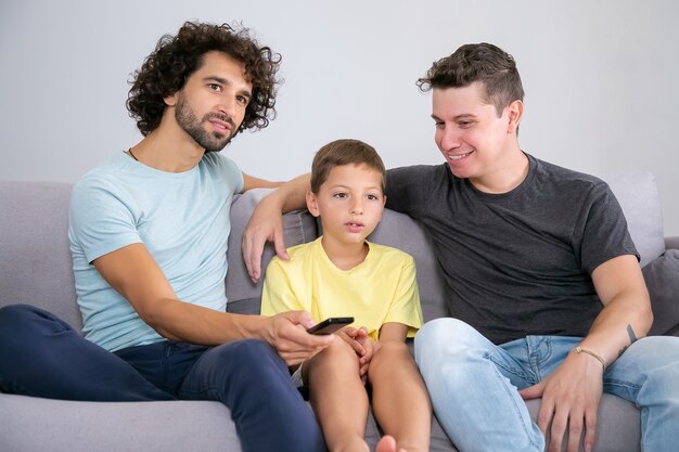 흥분된 소년과 그의 쾌활한 아빠는 집에서 TV 쇼를보고, 거실에서 소파에 앉아, 포옹, 리모컨을 사용하여 멀리보고. 가족 및 홈 엔터테인먼트 개념