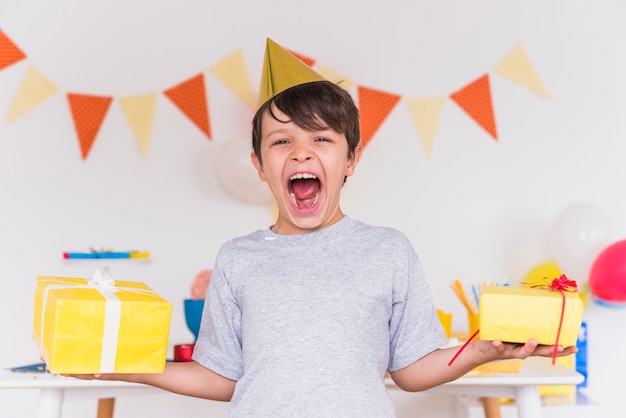 Excited boy with is mouth open holding birthday presents in hand