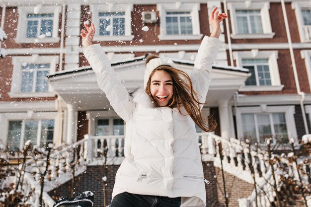 Excited brightful emotions of joyful pretty young woman on street in winter time. Raising hands, happiness, positivity, joy, winter holidays.