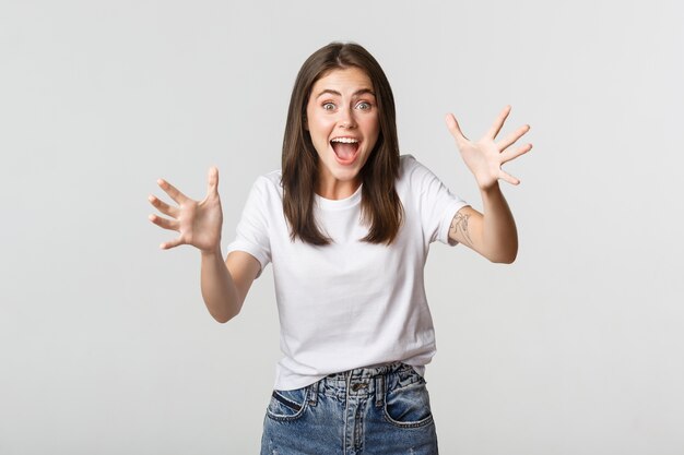 Excited brunette girl smiling amazed and raising hands to catch something.