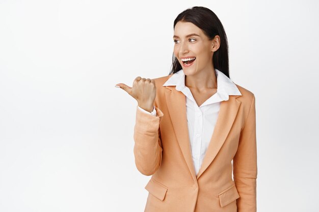 Excited brunette office manager pointing and looking left as laughing and smiling showing logo chart or diagram aside standing over white background