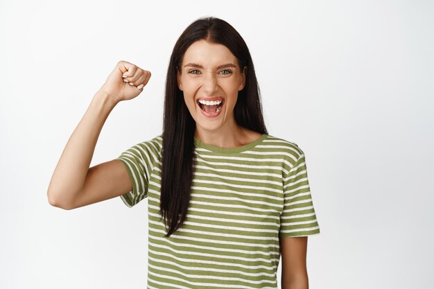 Excited brunette woman chanting female activist protesting raising clenched fist up and shouting with joyful face white background