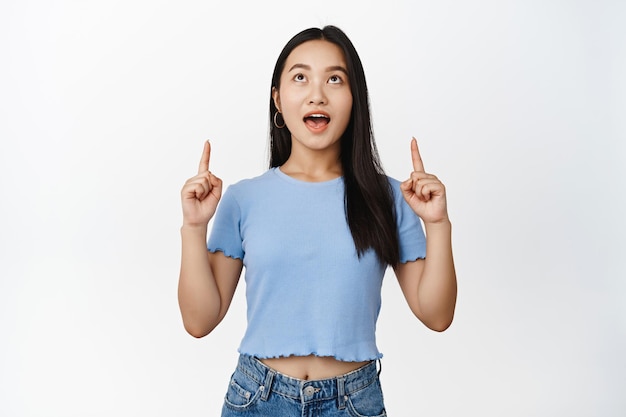 Excited brunette woman pointing and looking up with amazement checking out big news showing advertisement white background