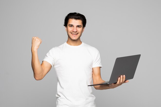 Excited business man looking at laptop screen with mouth wide open, celebrating his win on gray