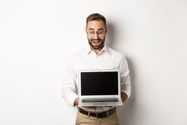 Excited businessman showing something on laptop screen, standing happy  