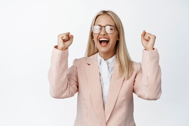 Excited businesswoman winning, chanting and screaming happy, celebrating victory, standing on white. Copy space