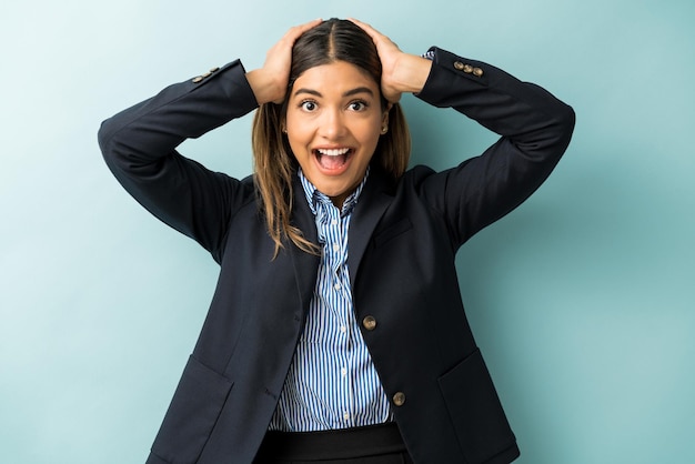 Excited businesswoman with head in hands standing surprised against blue background