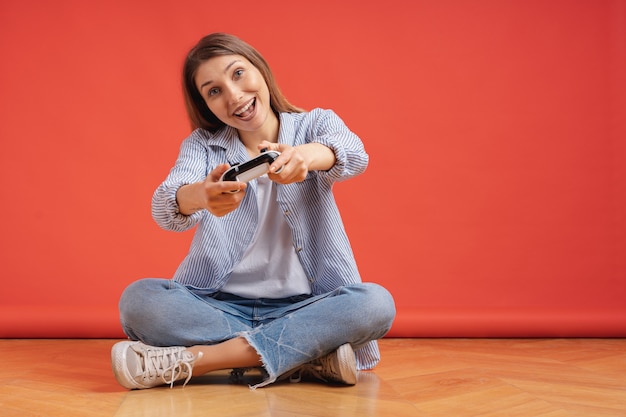 Excited casual young woman playing video games having fun on red
