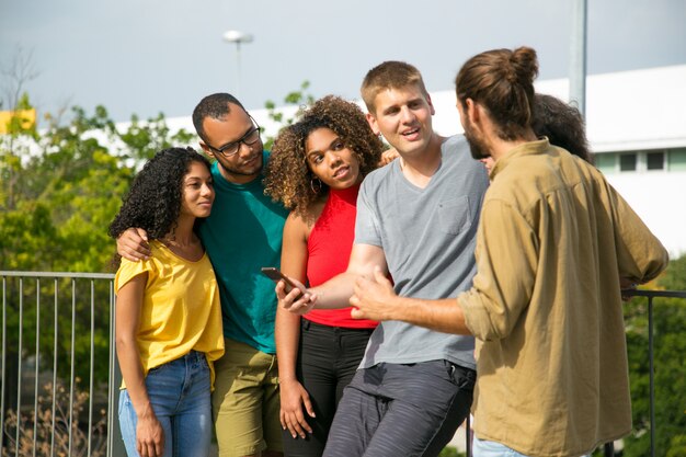 Excited Caucasian guy with smartphone arguing with male friend