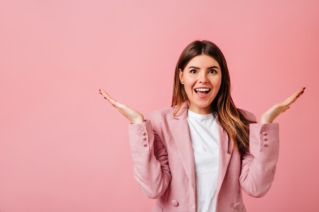 Excited caucasian lady standing with hands up. Studio shot of pretty brunette woman isolated on pink background.