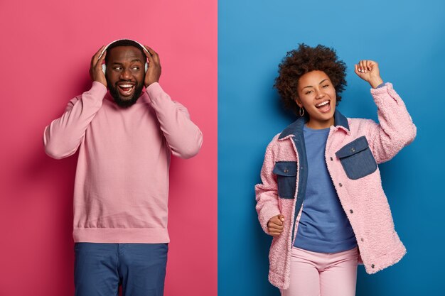 Excited cheerful black man and his girlfriend have fun on disco floor, dance to rhythm of music, wear wireless headphones, chilling and vibing indoor, spend free time at awesome party or festival