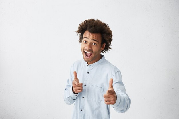 Excited cheerful man wearing light blue shirt raising eyebrows and exclaiming