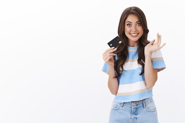 Free photo excited cheerful modern woman hold credit card and gesturing delighted, smiling broadly, boyfriend gave password to bank account lots of money, about to waste cash, paying online stores, shopping