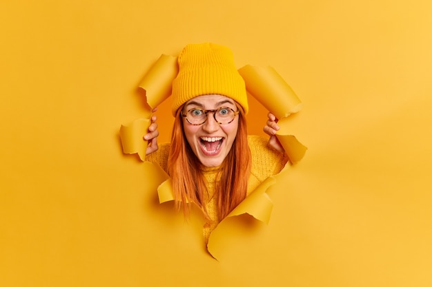 Free photo excited cheerful redhead millennial woman stares surprisingly has overjoyed expression keeps mouth opened wears trendy bright hat transparent glasses.