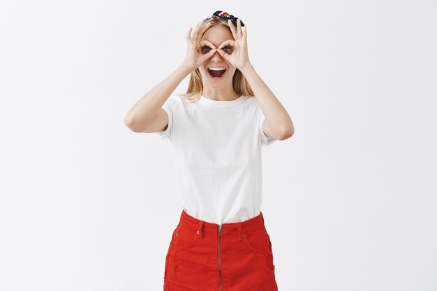 Excited cheerful young blond girl posing against the white wall