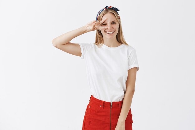 Excited cheerful young blond girl posing against the white wall