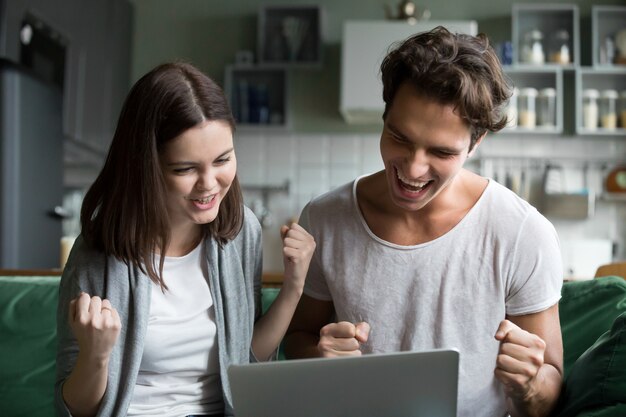 Excited couple ecstatic by online win looking at laptop screen 