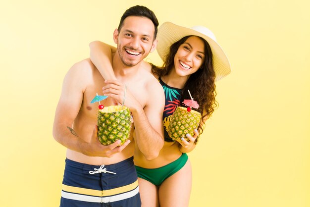 Excited couple in love hugging and laughing while drinking a pina colada cocktail during their relaxing honeymoon at a tropical resort