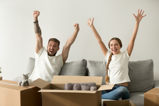 興奮しているカップルは新しい家に移動して幸せな手を上げて