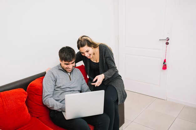 Excited couple sitting on sofa looking at laptop screen