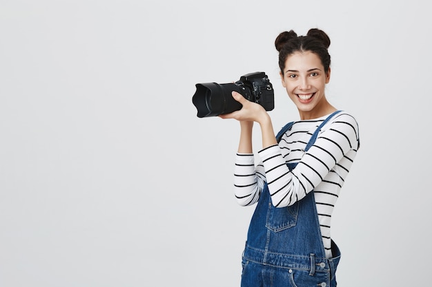 Excited creative female photographer taking pictures on camera, looking amused while photographing