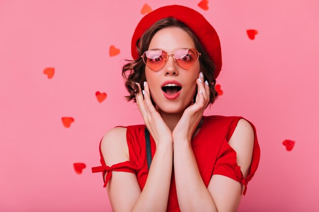 Excited cute girl posing with mouth open. Indoor shot of brunette lady in red beret.