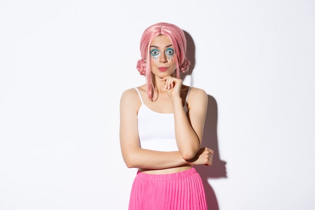 Excited cute party girl with pink wig and halloween makeup, looking with interest at camera, listening to something, standing.