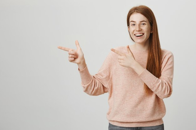 左の指を指している興奮したかわいい赤毛の10代の少女