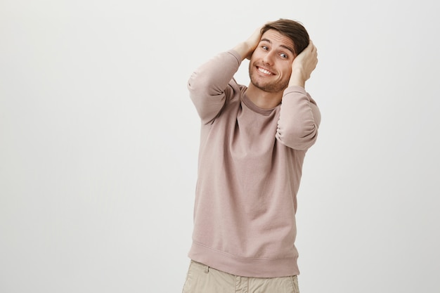 Excited cute young man hold hands on head and smiling silly