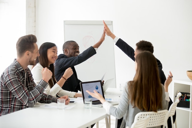 Excited diverse colleagues or partners giving high-five at team meeting