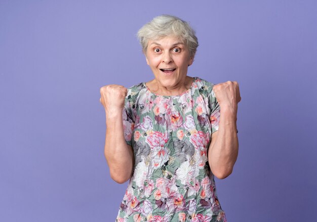 興奮した年配の女性は、紫色の壁に孤立した拳を探し続けます