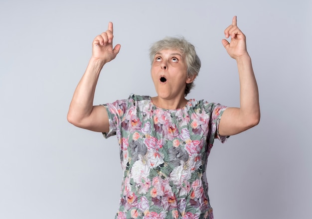 Free photo excited elderly woman looks and points up with two hands isolated on white wall