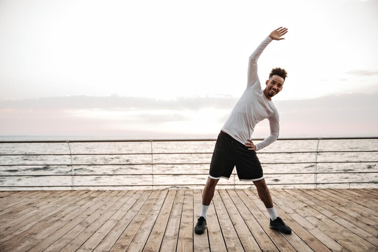 Free Photo excited energized brunette man in black shorts and longsleeved tshirt stretches and works out in good mood near sea