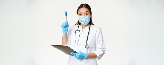 Excited female doctor asian physician holding clipboard and raising pen up found solution or idea standing in medical face mask over white background