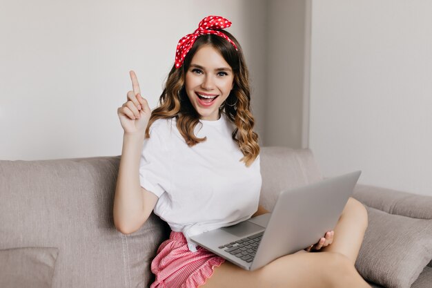 Excited female freelancer working at home. Indoor photo of amazing curly lady sitting on couch in cozy room.