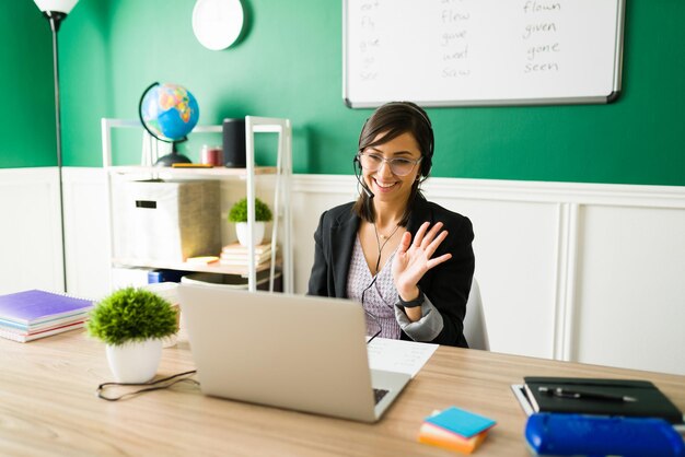 Excited female teacher with a headset waving hello to her students and smiling during a virtual class