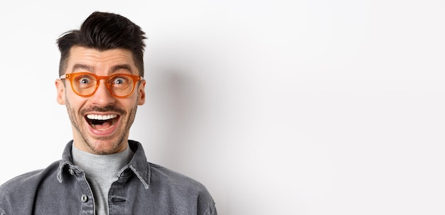 Free photo excited funny man in glasses smiling look with amazement and joy at awesome promo standing happy aga