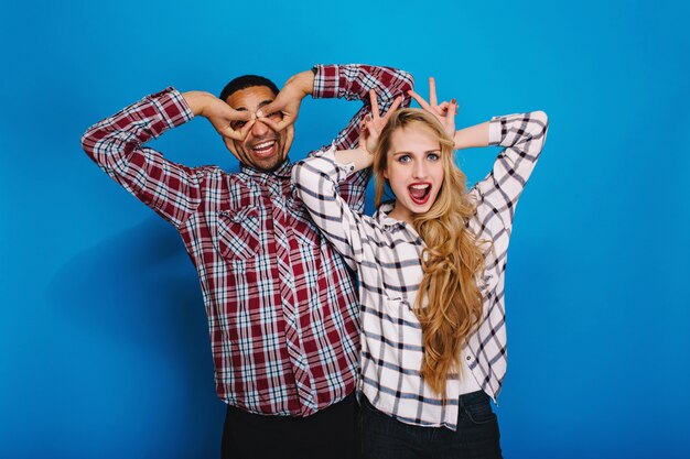 Excited funny young woman with long blonde hair having fun with handsome guy fooling around together. Expressing true brightful positive emotions, smiling, free time.