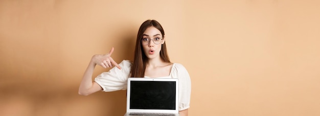 Free photo excited girl in glasses making presentation on computer pointing hand at laptop screen and say wow s