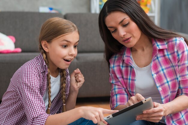 Excited girl pointing finger on digital tablet shown by female psychologist