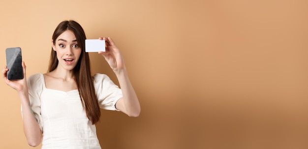 Free photo excited girl showing plastic credit card of bank and empty mobile phone screen demonstrate shopping