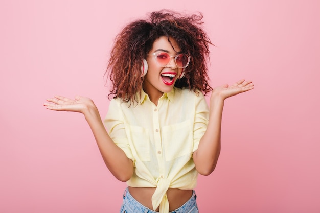 Free photo excited girl with african hairstyle posing emotionally. surprised mulatto lady wears vintage yellow shirt and blue jeans chilling