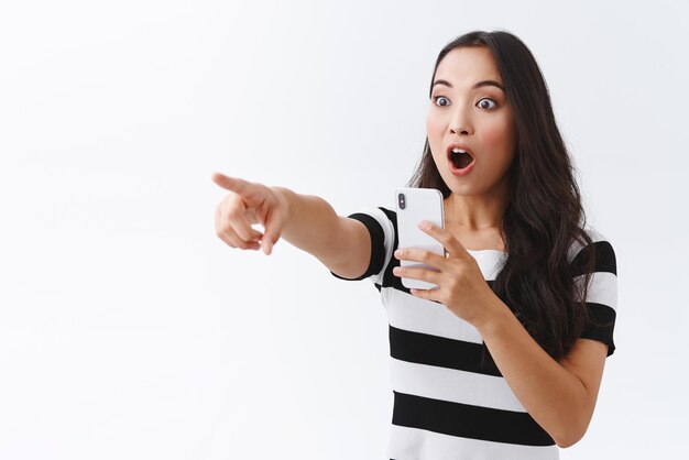 Excited girl witness something extremely awesome record video on smartphone camera pointing and staring impressed sideways gasping drop jaw astonished standing white background