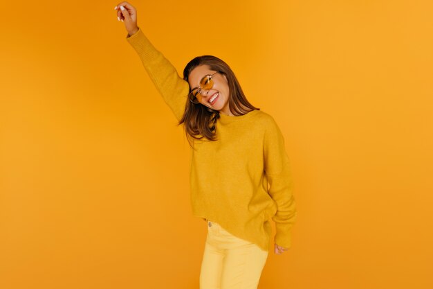 Excited girl in yellow pants expressing sincere emotions. Good-looking young lady in sunglasses fooling around .