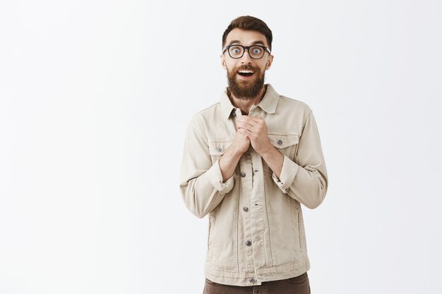 Excited and glad bearded man in glasses posing against the white wall