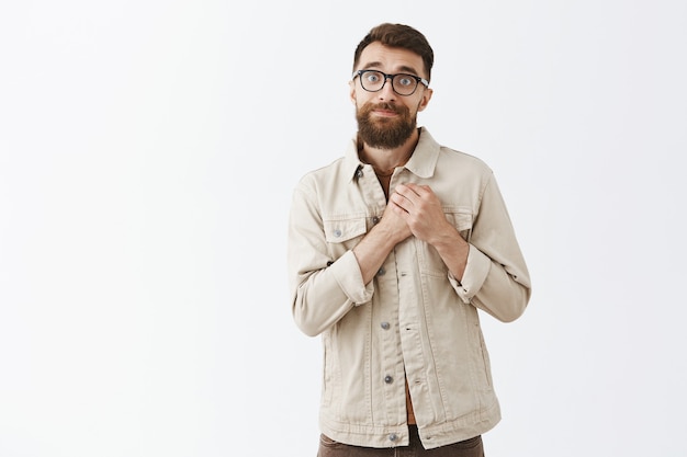 Excited and glad bearded man in glasses posing against the white wall